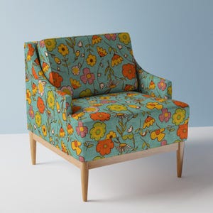 May include: A teal armchair with wooden legs upholstered in a floral fabric with orange, yellow, and pink flowers on a white background.