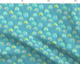 May include: A teal blue fabric with a repeating pattern of colorful rainbows. The rainbows are painted in shades of blue, green, yellow, and purple. The background is speckled with small black dots.