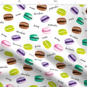 Puede incluir: Un patrón sin costuras que presenta ilustraciones de acuarela de macarons en varios colores y sabores, incluyendo pistacho, menta, chocolate, frutos rojos y lavanda. Los macarons están dispuestos en un patrón aleatorio sobre un fondo blanco, con los nombres de los sabores escritos en letra cursiva negra.