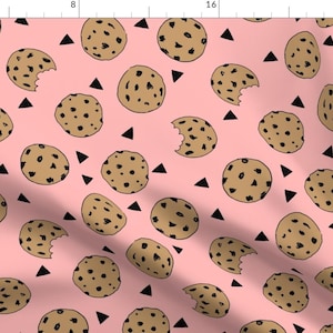 May include: A pink fabric with a repeating pattern of brown chocolate chip cookies and black triangles.