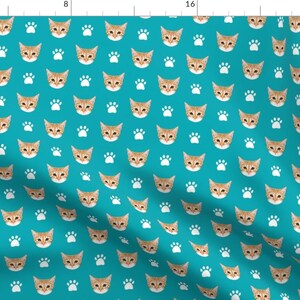 May include: A teal blue fabric with a repeating pattern of orange cat faces and white paw prints.