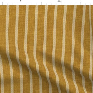Può includere: Tessuto giallo senape con strisce verticali bianco sporco. Le strisce sono uniformemente distanziate e corrono per tutta la lunghezza del tessuto. Il tessuto ha un aspetto strutturato, che suggerisce una trama di lino o simile. Questo motivo è adatto per l'arredamento della casa o l'abbigliamento.