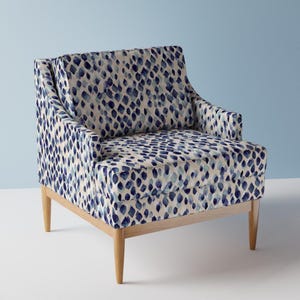 Könnte beinhalten: Ein blauer und weißer Sessel mit Holzbeinen. Der Sessel hat eine gepolsterte Rückenlehne und einen bequemen Sitz.