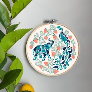 Könnte beinhalten: Ein runder Stickrahmen mit weißem Hintergrund und einem farbenfrohen Design aus einem Pfau und einem Elefanten, umgeben von grünen Blättern und rosa Erdbeeren.