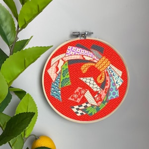 May include: A red embroidery hoop with a colorful Japanese-inspired design featuring geometric patterns and a yellow bow. The design is made up of various fabrics with different textures and patterns.