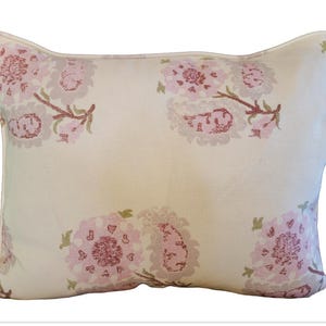 May include: Cream-colored rectangular pillow with a floral pattern in shades of pink and brown. The pillow has a unique shape with curved edges and a soft, inviting appearance. The floral design is repeated across the surface.