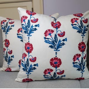 Puede incluir: Dos almohadas blancas con un patrón floral. Las almohadas presentan flores rosas y azules con hojas verdes sobre un fondo blanco.
