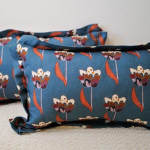 May include: Two rectangular throw pillows featuring a blue fabric base with a repeating pattern of stylized tulips in shades of white, dark purple, and orange. Each pillow has a ruffled flange edge detail and a soft, filled construction.