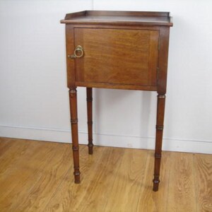 May include: A wooden side table with a single door and a brass handle. The table has four slender legs.