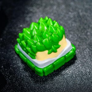 Peut inclure: Un capuchon de touche vert et blanc avec un design en relief piquant ressemblant &agrave; un fruit du durian. Le capuchon de touche est en plastique et a une base blanche avec un dessus vert.