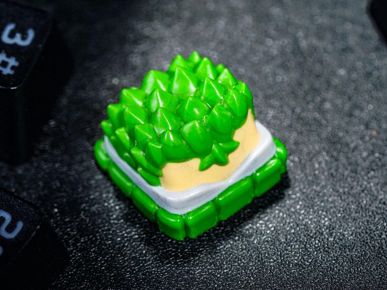 Peut inclure: Un capuchon de touche vert et blanc avec un design en relief piquant ressemblant &agrave; un fruit du durian. Le capuchon de touche est en plastique et a une base blanche avec un dessus vert.