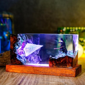 Könnte beinhalten: Ein rechteckiges Kunstwerk aus Harz mit Star Wars-Motiv. Es zeigt ein Miniaturraumschiff, eine Darth Vader-Figur mit rotem Lichtschwert und einen Holzsockel. Das klare Harz hat violette und blaue Akzente.