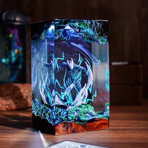 Op de afbeelding: Een rechthoekige hars sculptuur met een superheld figuur met blauwe en witte accenten, omringd door blauwe bliksemeffecten. De basis is een mix van hout en hars, met een donkere achtergrond.