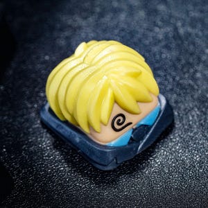 Peut inclure: Un capuchon de touche jaune et bleu avec un personnage de dessin anim&eacute; aux cheveux jaunes h&eacute;riss&eacute;s et un motif en spirale sur le visage.