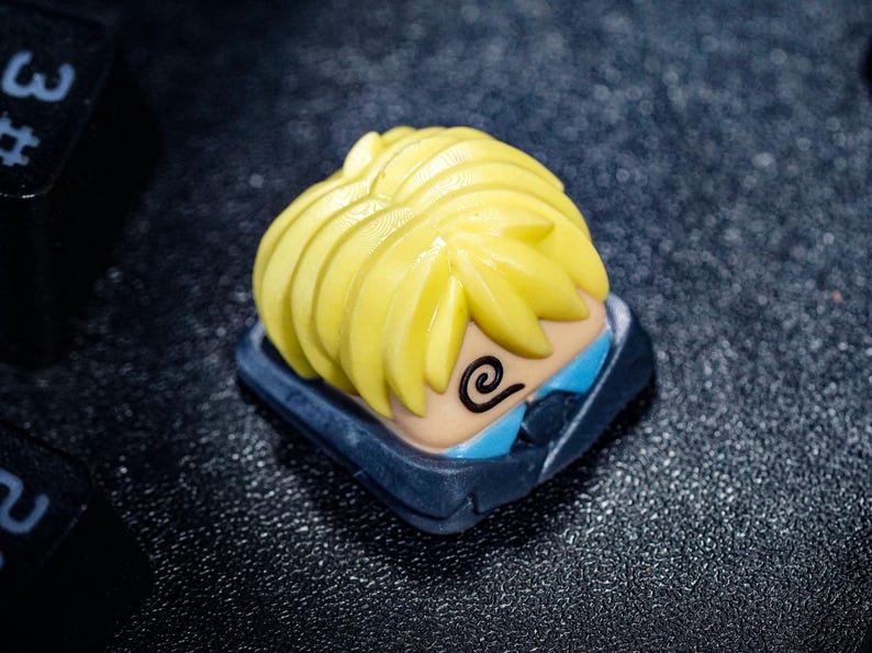 Peut inclure: Un capuchon de touche jaune et bleu avec un personnage de dessin anim&eacute; aux cheveux jaunes h&eacute;riss&eacute;s et un motif en spirale sur le visage.