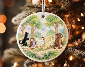 May include: A round white ceramic ornament featuring a watercolor illustration of a black and white cat, an owl, a white chicken, a yellow duck, and a brown bear walking in a line through a forest. The text Emily 2026 is printed at the bottom.
