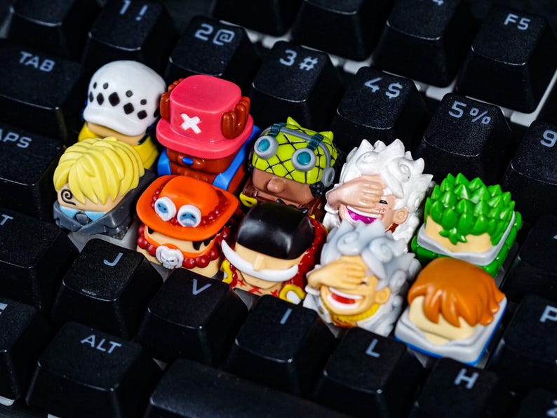 Peut inclure: Un ensemble de dix touches de clavier color&eacute;es repr&eacute;sentant des personnages de dessins anim&eacute;s avec diff&eacute;rentes expressions faciales. Les touches sont dispos&eacute;es sur un clavier noir.