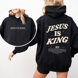 May include: Black hoodie with the text "JESUS IS KING" on the front and back. The back design includes the text "JESUS IS KING" with a crown graphic and a Bible verse. The hoodie is a casual, comfortable garment.