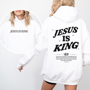 May include: White hoodie with the text "JESUS IS KING" on the front and back. The back design includes the words "JESUS IS KING" with a crown graphic and a Bible verse. A casual, religious-themed apparel item.