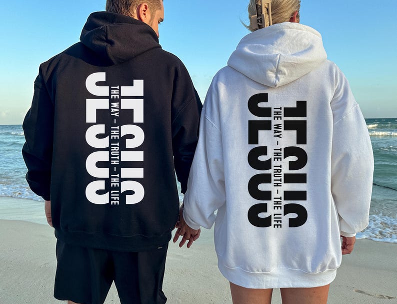 May include: Black and white hoodies featuring the word "JESUS" printed vertically on the back, with the text "THE WAY - THE TRUTH - THE LIFE." Two people are seen wearing the hoodies while standing on a beach.