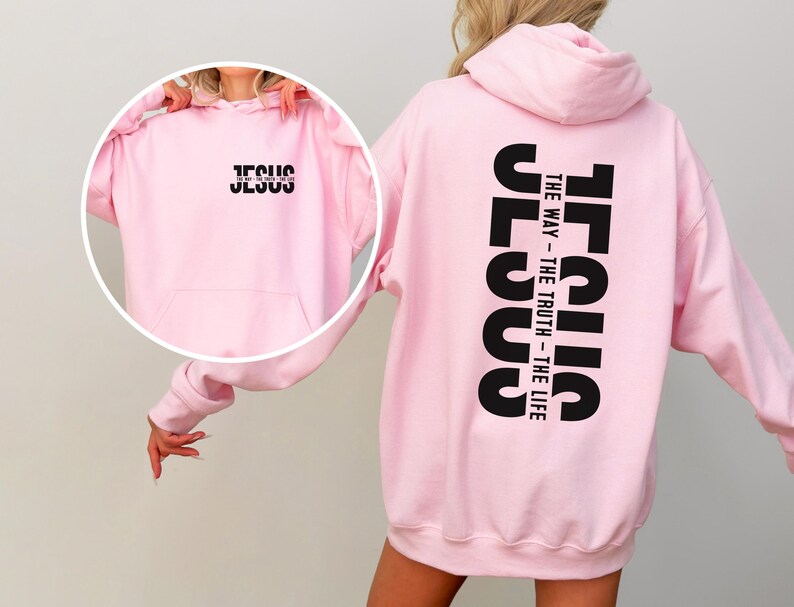 May include: A pale pink hoodie featuring the word "JESUS" in black on the front and the words "JESUS THE WAY - THE TRUTH - THE LIFE" printed vertically on the back. The hoodie has a hood and a front pocket.