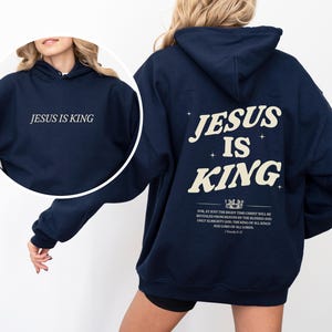 May include: Navy blue hoodie with the text "JESUS IS KING" on the front and back. The back design includes the words "JESUS IS KING" in a stylized font, along with a Bible verse. The hoodie is a casual garment.