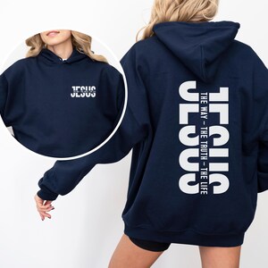 May include: Navy blue hoodie with white text. The front of the hoodie has the word "JESUS" printed in white. The back of the hoodie has the word "JESUS" vertically, with "THE WAY - THE TRUTH - THE LIFE" printed below.