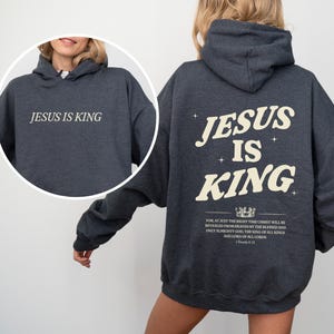 May include: Dark gray hoodie with the text "JESUS IS KING" on the front and back. The back design includes the text "JESUS IS KING" in a stylized font, along with additional text and a crown graphic.