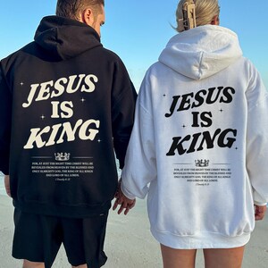 May include: Black and white hoodies with the text "JESUS IS KING" printed on the back. The hoodies also feature a quote from 1 Timothy 6:15. The image shows two people wearing the hoodies at the beach.