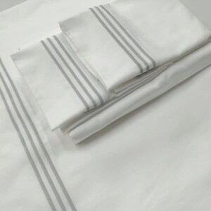 May include: A set of white bed linens with gray stripes. The linens are folded and stacked on top of each other.