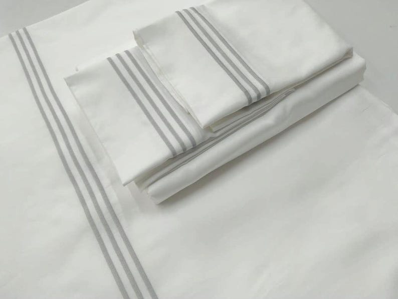 May include: A set of white bed linens with gray stripes. The linens are folded and stacked on top of each other.