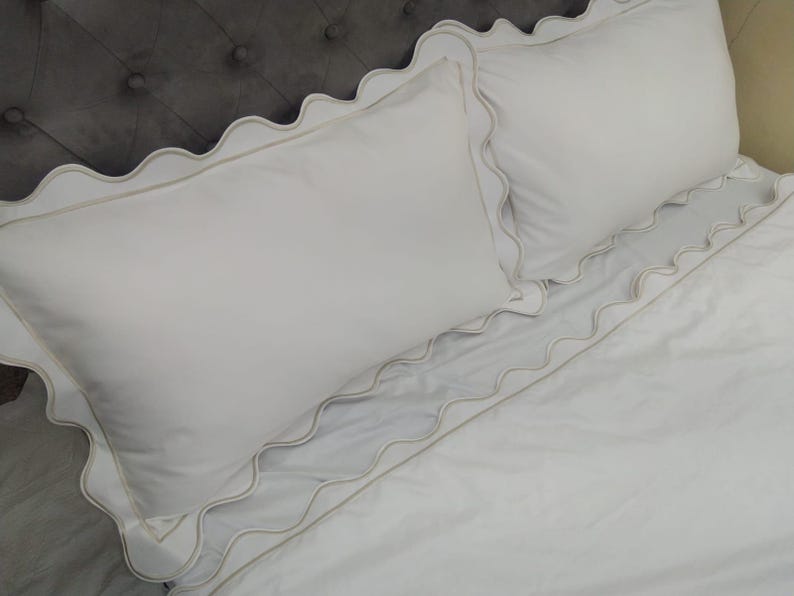 May include: White bedding with a scalloped edge. The bedding is made of a soft, smooth fabric and has a subtle sheen.