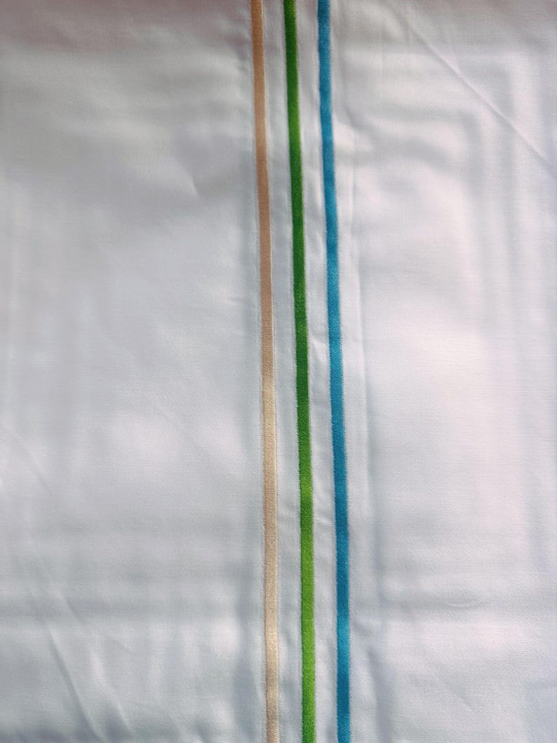 K&ouml;nnte beinhalten: Wei&szlig;er Stoff mit drei vertikalen Streifen an der Seite. Die Streifen sind beige, gr&uuml;n und blau.