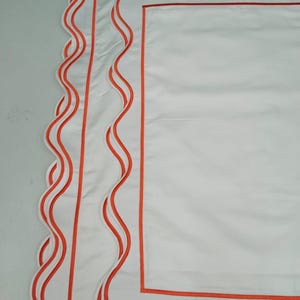 May include: White pillowcase with a scalloped edge and three orange trim lines.