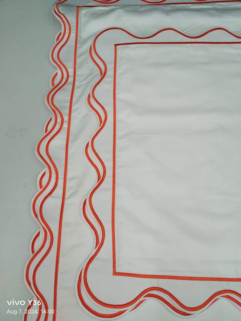 May include: White pillowcase with a scalloped edge and three orange trim lines.