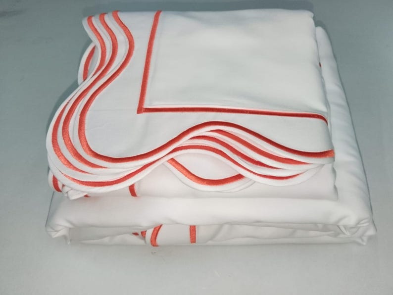 May include: A set of white bed linens with a scalloped edge and a coral colored trim.