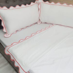 May include: White bedding with a red scalloped trim. The bedding is made of a soft, comfortable fabric and is perfect for a bedroom.