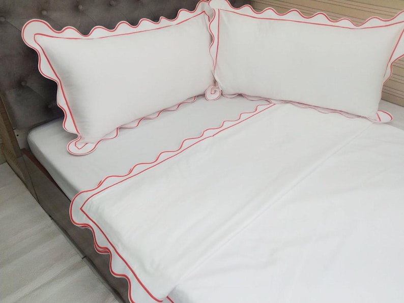 May include: White bedding with a red scalloped trim. The bedding is made of a soft, comfortable fabric and is perfect for a bedroom.