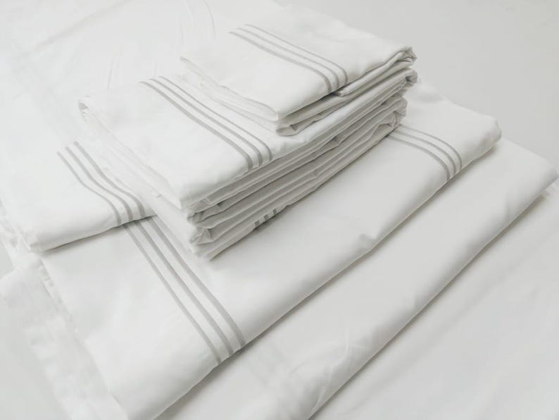 May include: A stack of white bed sheets with gray stripes. The sheets are folded neatly and are ready to be used.