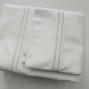 May include: White bed sheet set with a subtle gray stripe detail. The sheet set includes a flat sheet, fitted sheet, and pillowcases.