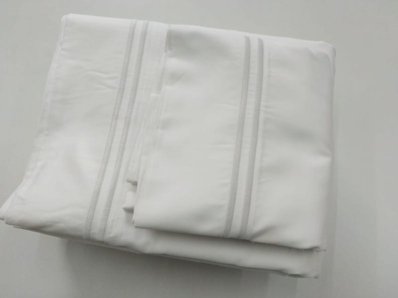 May include: White bed sheet set with a subtle gray stripe detail. The sheet set includes a flat sheet, fitted sheet, and pillowcases.