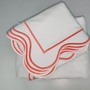 May include: A stack of white bed linens with a coral colored scalloped edge.