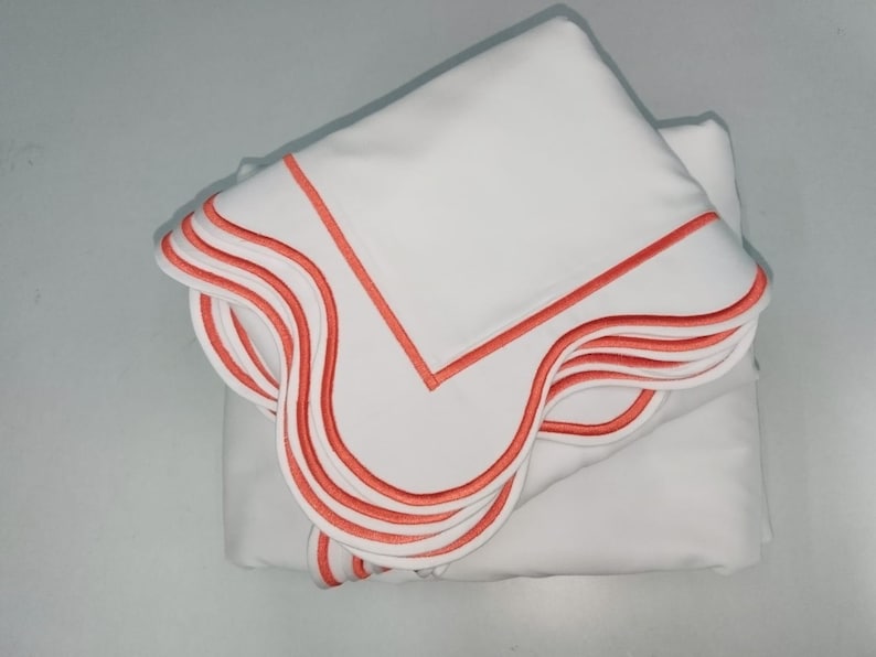 May include: A stack of white bed linens with a coral colored scalloped edge.