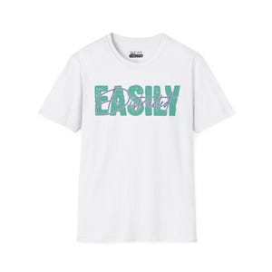 May include: A white short-sleeve t-shirt featuring the word EASILY in large, textured teal block letters with the word Distracted written in a purple cursive script overlaying the centre. The inner neck label displays the text WEAR TRUTH.