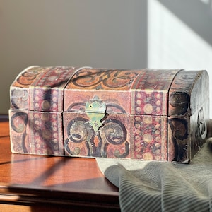 May include: A vintage wooden chest with a curved top and ornate, patterned design in shades of red, brown, and gold. The chest features a decorative metal clasp and hinges, suggesting a storage or decorative function.