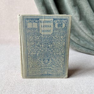 May include: A vintage book with a blue and white floral design on the cover. The title is "Blackmore's Lorna Doone" and the book is part of the "Macmillan's Pocket Classics" series.