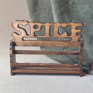 May include: A wooden spice rack with the word "SPICE" cut out at the top. The rack has two shelves and is made of dark brown wood. The rack is designed to hold spice jars and is a decorative kitchen item.