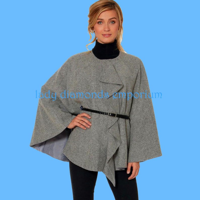 May include: A grey cape-style coat with a black belt. The coat has an asymmetrical design and is worn over a black turtleneck. The text "lady diamonds emporium" is visible on the coat.