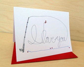 May include: A white card with a red envelope. The card features a black and white illustration of a fishing rod with a line that forms the words "I love you". There are small red hearts along the line.