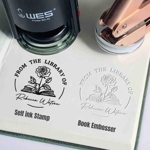 May include: A black self-inking stamp and a rose gold book embosser. Both have a design of a rose and an open book with the text "From the Library of" and a space for a name. The stamp says "Self ink Stamp" and the embosser says "Book Embosser".